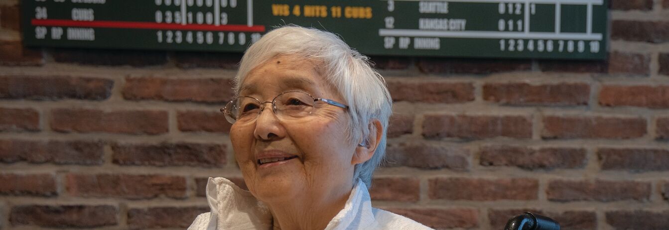 A smiling senior resident with a brick background.